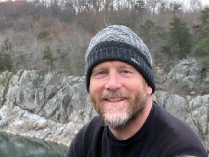 smiling man with trees and rocky cliffs in background