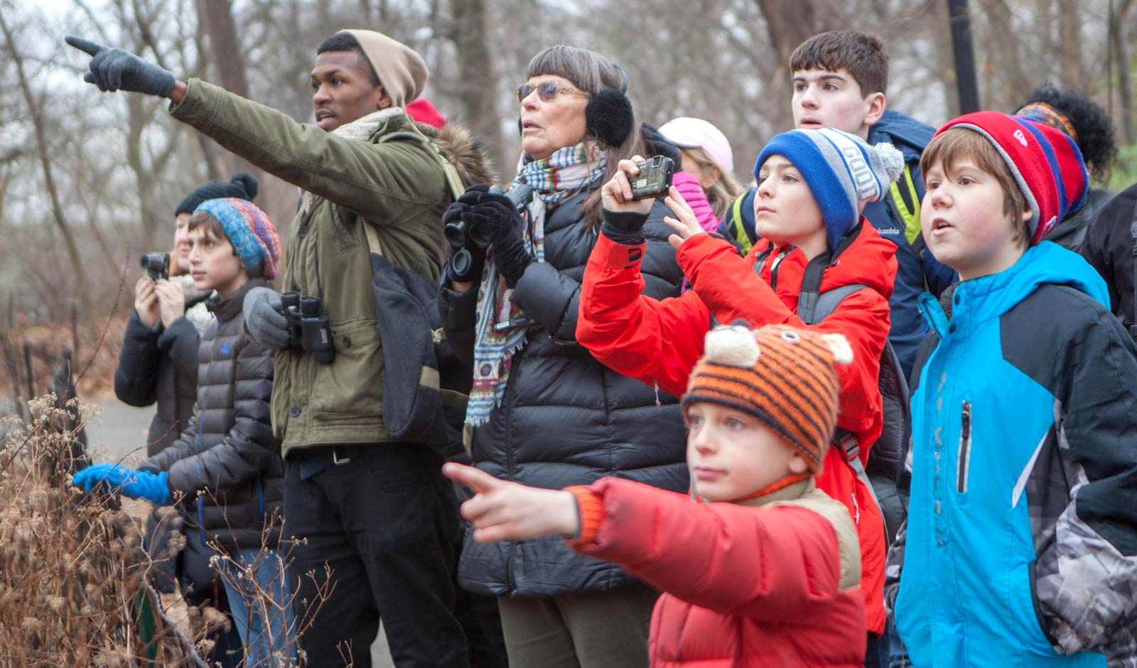 Two adults lead a group of kids and point out a bird in front of them