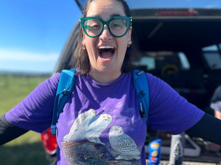 Excited woman with green glasses and purple Tshirt with owls on it.