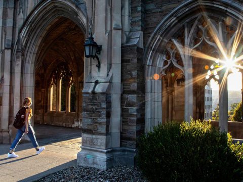 Student walking below arches at Cornell