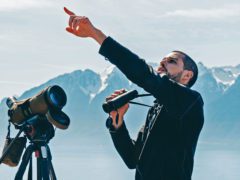 Raphaël Nussbaumer points to a bird with a mountain backdrop
