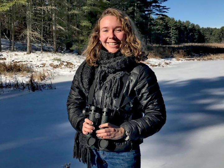 Sarah Hooghuis stands in the sun and snow with binoculars.