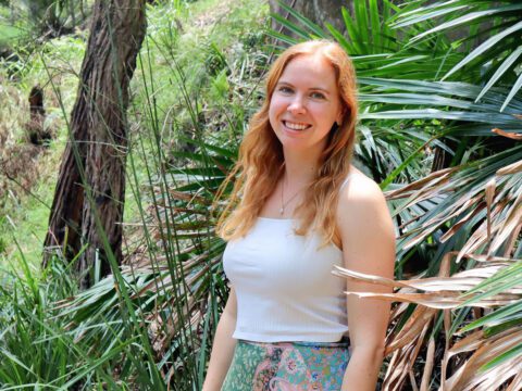 a woman stands surrounded by tropical plants.