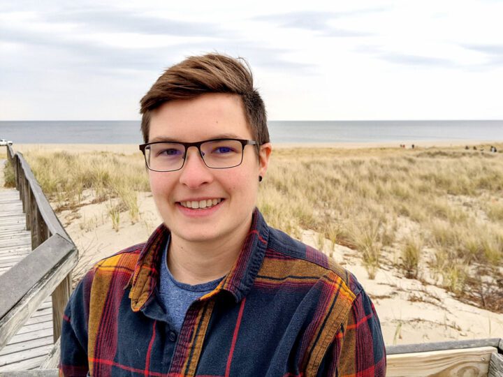 Person stands in front of seaside dunes.