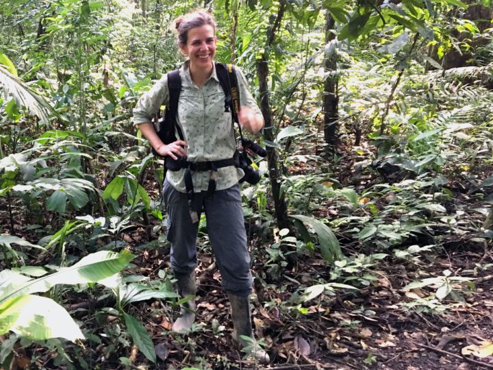 A woman stands in a tropical wood with a backpack on