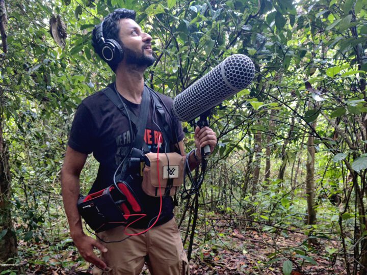 A man stands in a forest with recording equipement.