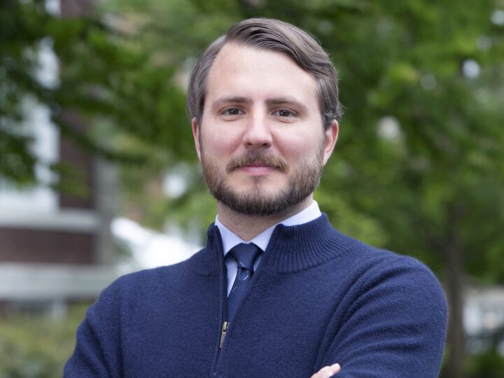 Nab with beard in blue sweater, trees in background.