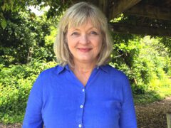 Lady in bright blue shirt with bushes in background.