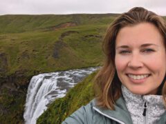 Woman stands in front of a green, hilly landscape