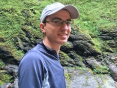 Man with cap and glasses standing in nature.