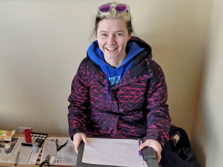 Smiling girl with clipboard and purple sunglasses on head.