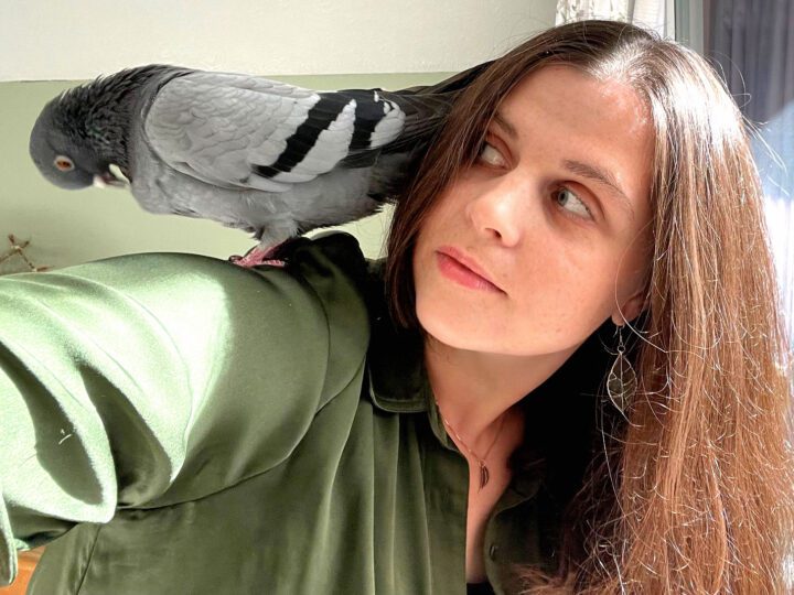 Woman with long hair and her pet pigeon on her shoulder.