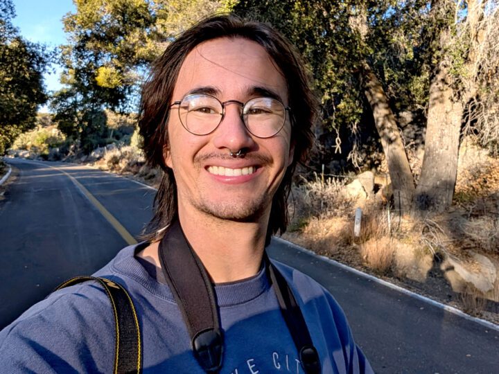 Smiling man with glasses looks into the camera with a road in the background.