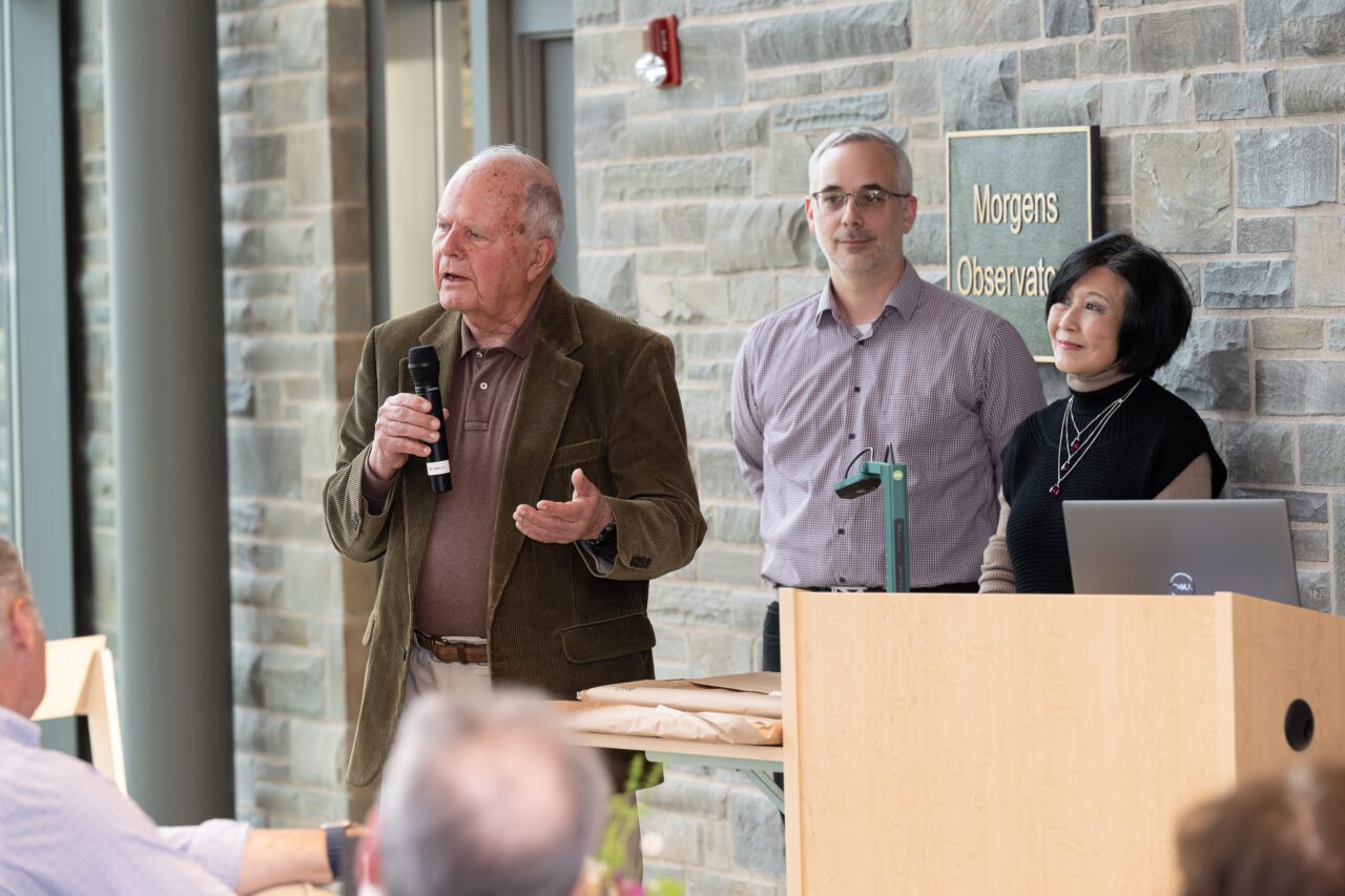 Charles Walcott speaking into a microphone with Holger Klinck and K. Lisa Yang standing behind.
