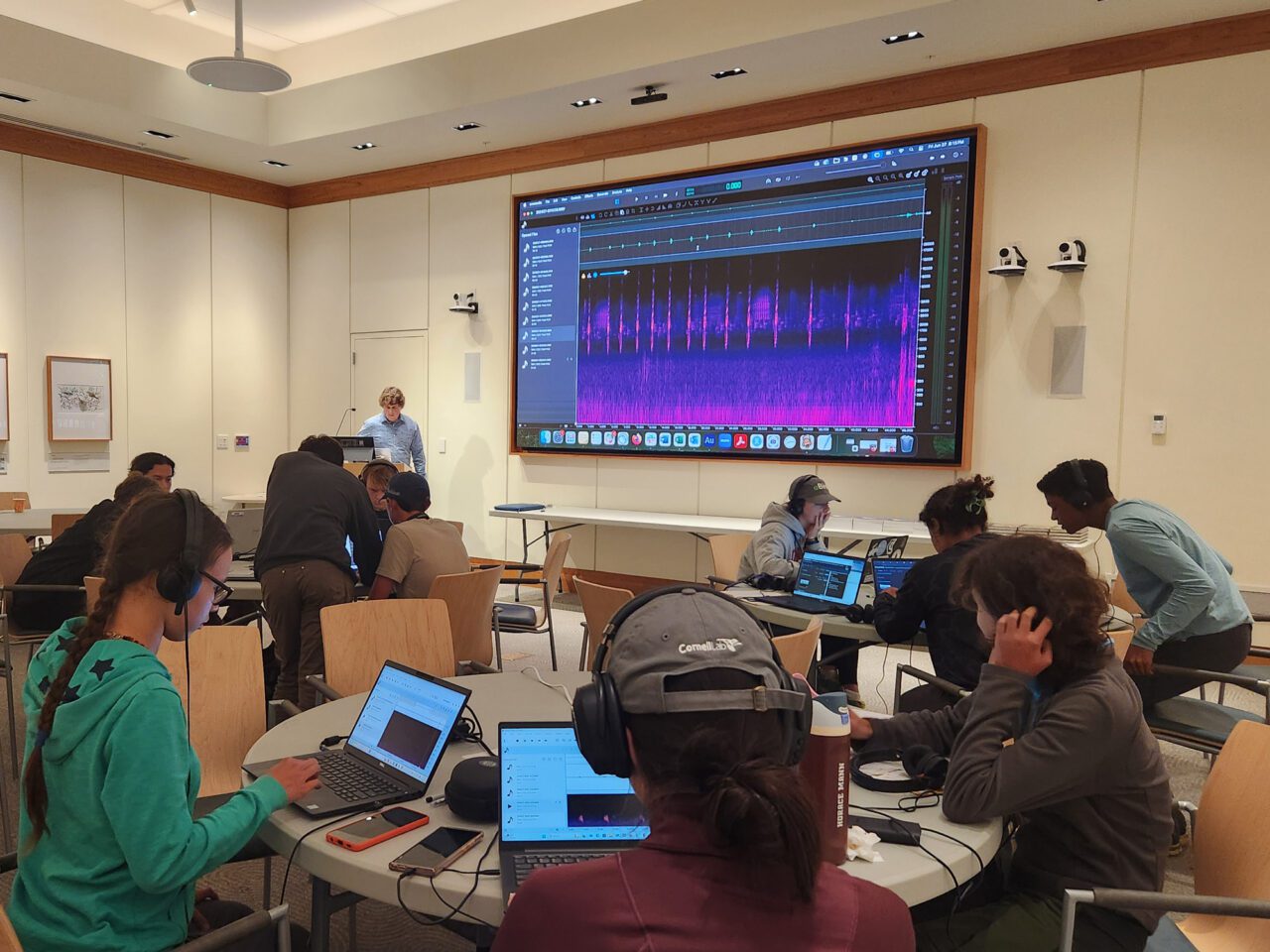 students using laptops and headphones in a classroom with an audio spectrogram on screen