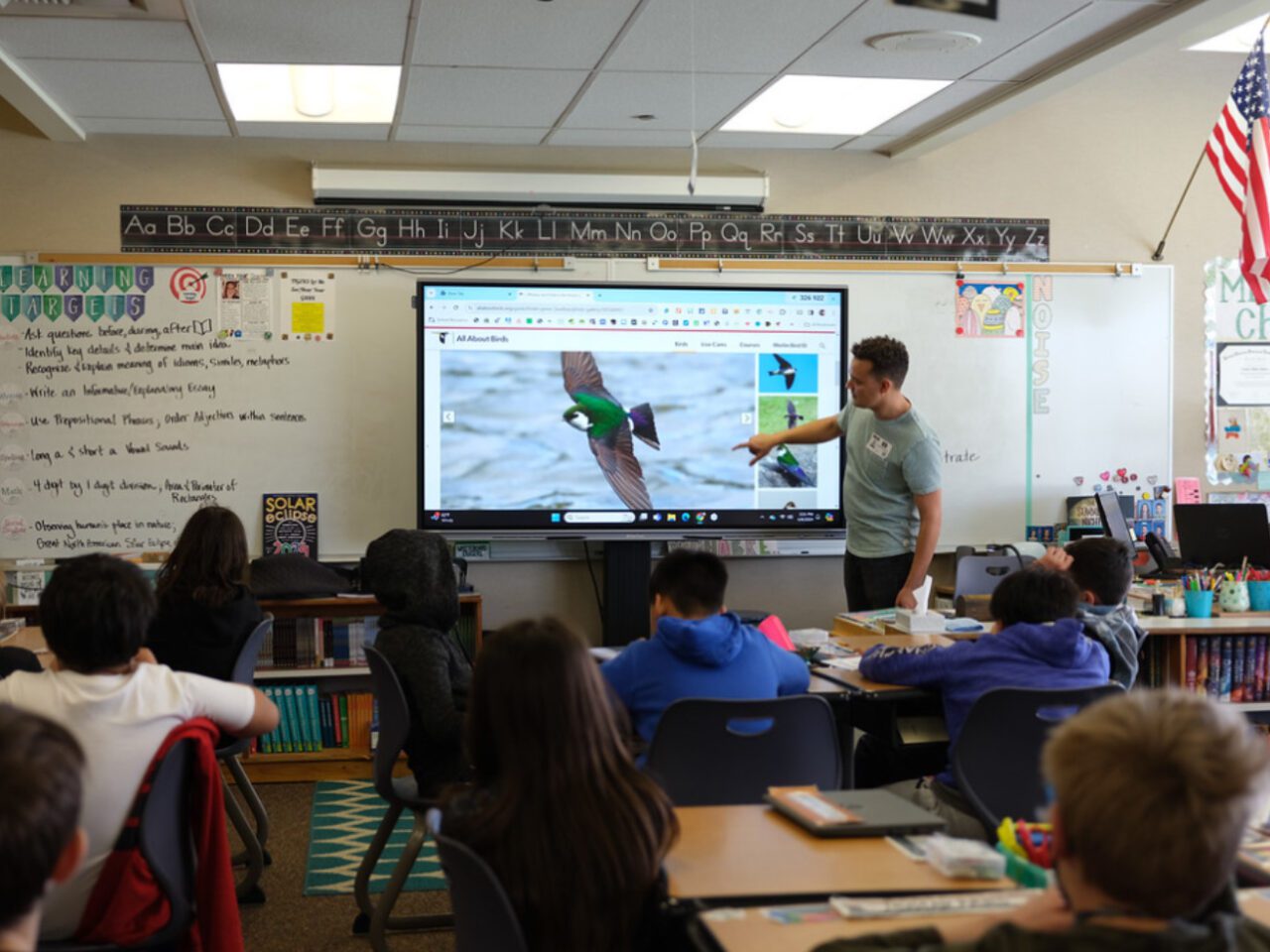 Teacher pointing at a bird photo on a classroom screen while students watch from their desks
