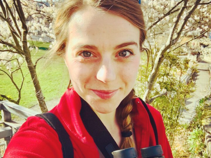 Olivia looking at the camera while holding binoculars in nature