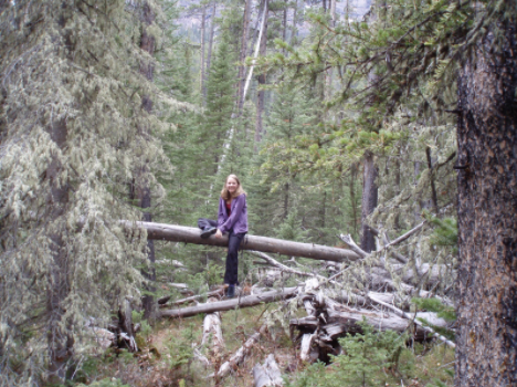 Photo of Kira Klebe sitting on a tree that had fallen in the woods.