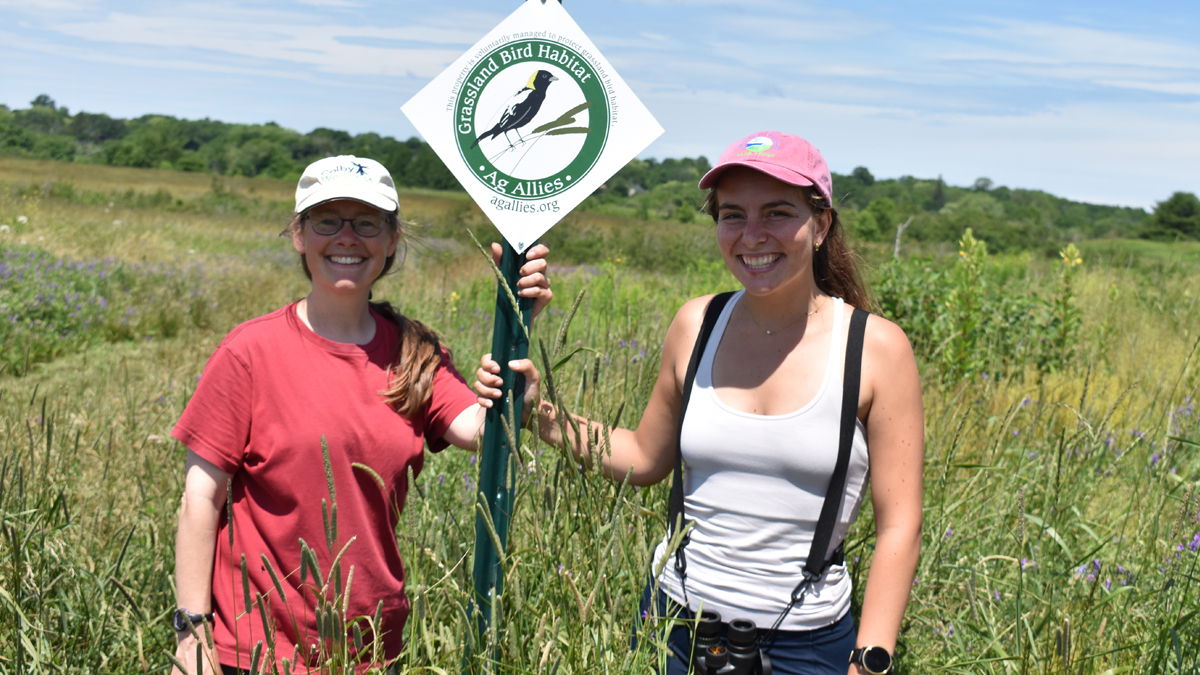 Two Women Holding Grassland Bird Sign in Field