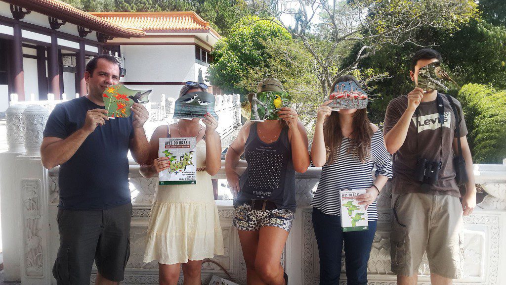 La gente posa sosteniendo fotografías de pájaros sobre sus ojos.