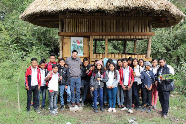 A group of school children and teachers stand in front of a bird viewing gazebo