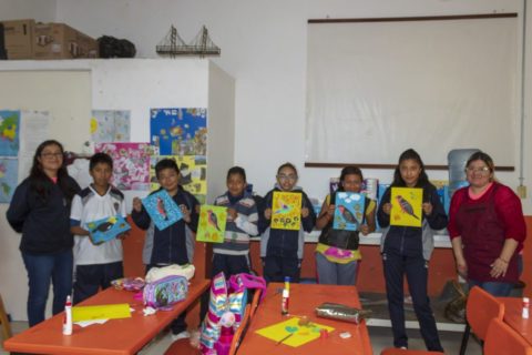 A group of students hold up their colorful bird paintings