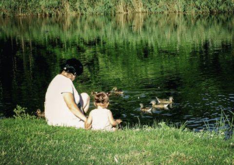 A woman and toddler next to a lake with ducks