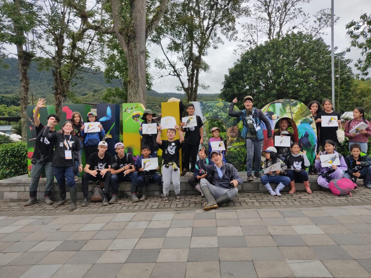 Kids and adults standing in front of a sign holding up handmade bird drawings