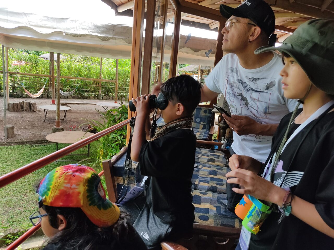 Children and an adult observing birds with binoculars from a balcony