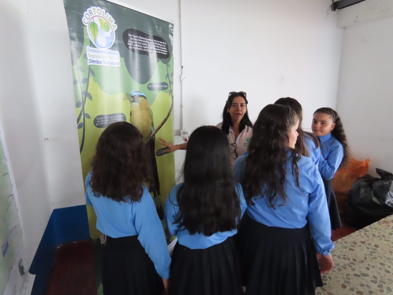 There are five students standing around a woman who is discussing the poster presented in front of them.
