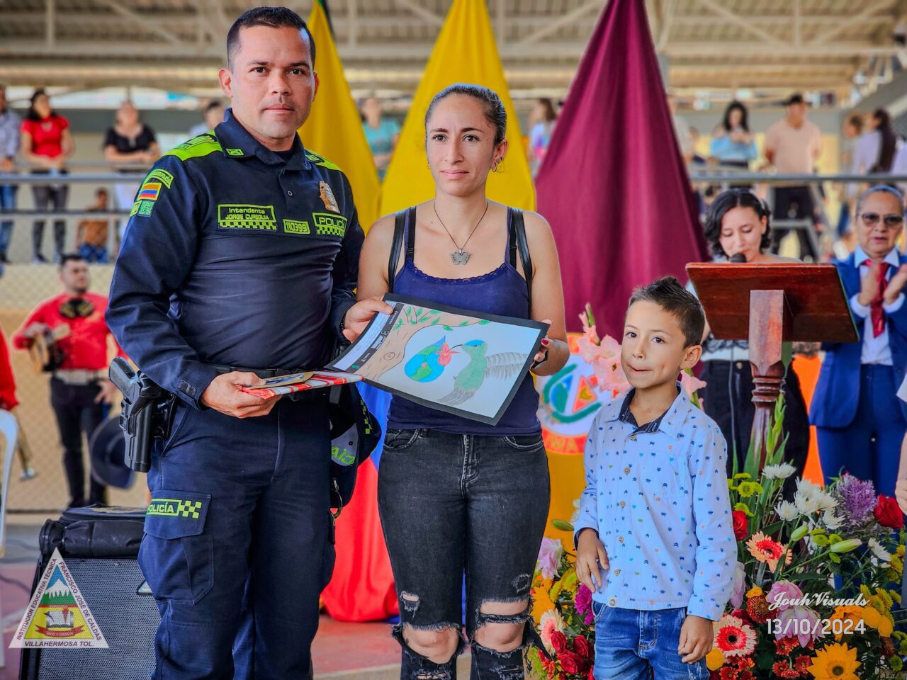 There are two adults and one child facing the camera. The woman in the middle is showcasing her bird illustration.